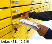 A hand retrieves mail from a bright yellow mailbox in an apartment complex. Concept of: Receiving messages. Стоковое фото, фотограф Ольга Петрова-Апостолова / Фотобанк Лори