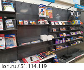 In an electronics and office supplies store. The shelves are filled with various storage media and consumables: CD-R and DVD-R compact discs, Verbatim and other brand disc packaging, envelopes and storage boxes, laminating film, photo paper for the printer, as well as recording and printing accessories. The shelves are partially filled, some of the cells remain empty, which emphasizes the modern trend of the disappearance of physical storage media. The photo is well suited for illustrations related to technology, data storage, office supplies, retail outlets, and retro paraphernalia of the digital age. (2019 год). Редакционное фото, фотограф Анна Кривицкая / Фотобанк Лори