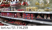 The shelves of the store are filled with New Year's decorations and Christmas tree balls. The display window features red, gold and white balls of different sizes and designs - matte, glossy, with glitter and patterns. The upper part contains hanging sets of toys, deer figurines and decorative elements. The abundance of festive decor creates an atmosphere of preparation for the New Year and Christmas. The photo is perfect for the theme of holidays, shopping, interior design, winter traditions and preparation for celebrations. (2018 год). Редакционное фото, фотограф Анна Кривицкая / Фотобанк Лори
