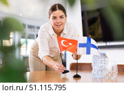 Positive young woman putting flag of Turkey on the table with flag of Finland in conference room. Стоковое фото, фотограф Яков Филимонов / Фотобанк Лори