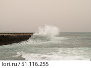 Powerful waves slamming pier during storm, generating massive water spray highlighting oceanic turbulence and maritime intensity. Стоковое фото, фотограф Данил Руденко / Фотобанк Лори