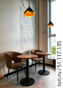 Modern cafe interior featuring stylish brown chairs and wooden tables, illuminated by warm pendant lights, creating a cozy atmosphere for relaxation and socializing. Редакционное фото, фотограф Елена Гоосен / Фотобанк Лори