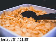 Close-up view of golden corn flakes filling a white ceramic bowl, accompanied by a black spoon, highlighting a quick and nutritious breakfast option perfect for busy mornings. Стоковое фото, фотограф Ольга Ильина / Фотобанк Лори
