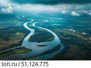 Sinuous river meandering through lush green landscape under dramatic sky. Стоковое AI-изображение, AI-художник Иван Рябоконь / Фотобанк Лори