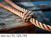 Nautical rope with knot securing boat to wooden dock. Стоковое AI-изображение, AI-художник Иван Рябоконь / Фотобанк Лори