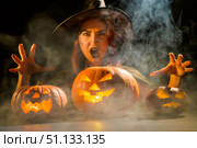 An ominous witch in a hat conjures over a jack-o-lantern. Traditional halloween characters. Mystical fog creeps over pumpkins with carved terrible faces. An evil witch casts a spell. Стоковое фото, фотограф Михаил Решетников / Фотобанк Лори