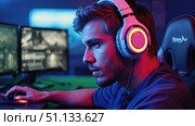 A focused gamer immersed in action, wearing high-tech headphones and using a gaming mouse in a vibrant, illuminated environment with multiple screens. Стоковое AI-изображение, AI-художник Владимир Федоров / Фотобанк Лори