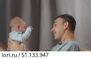A tender moment between father and child. A man pats the baby's nose with his finger, holds him in his arms and kisses him. A parent plays with his little son. Стоковое видео, видеограф Воловодов Владимир / Фотобанк Лори