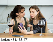 Two sad middle-aged women looking at the phone display while sitting at the table at home. Стоковое фото, фотограф Яков Филимонов / Фотобанк Лори