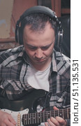 A musician plays an electric guitar, wearing headphones and a plaid shirt. The indoor setting suggests a casual jam session, filled with creativity and passion for music. Стоковое видео, видеограф Воловодов Владимир / Фотобанк Лори