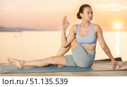 Calm european young female yoga trainer practicing Half Lord of fishes pose or Ardha Matsyendrasana during yoga training on seashore at sunrise. Стоковое фото, фотограф Яков Филимонов / Фотобанк Лори