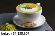 Steaming matcha and turmeric latte art displaying intricate patterns, served in white porcelain with slate coaster, garnished by fresh turmeric root and vibrant green powder. Стоковое AI-видео, аниматор Юрий Поздников / Фотобанк Лори