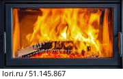 Intense radiant heat from bright orange and yellow flames engulfing glowing wood logs inside contemporary glass-fronted fireplace, providing cozy warmth and inviting ambiance. Стоковое AI-изображение, AI-художник Данила Большаков / Фотобанк Лори