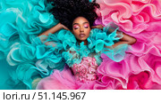 Enchanting woman with vibrant pink makeup and curly hair gracefully reclines amidst flowing ocean of voluminous fuchsia and turquoise ruffled fabric, creating serene and artistic dreamscape. Стоковое AI-изображение, AI-художник Данила Большаков / Фотобанк Лори