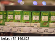 Supermarket shelves with herbs and spices from the Green Cuisine brand. In the foreground, neat green packages with transparent windows are visible through which you can see the contents: lime leaves, whole chilies, coriander seeds, chive flakes, ground cinnamon and nutmeg. Each box has a minimalist design with a white label indicating the country of origin of the product - Thailand, China, Morocco, Great Britain, India. At the bottom of the boxes are price tags with information about weight and cost. The photo conveys the atmosphere of a grocery store, demonstrates the variety of spices for cooking and emphasizes the organic and natural style of the brand. (2015 год). Редакционное фото, фотограф Анна Кривицкая / Фотобанк Лори