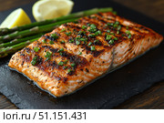 Grilled Salmon Fillet with a crispy skin, served with asparagus and lemon wedges on a black slate plate. Footage for culinary video blog. Стоковое AI-изображение, AI-художник Ирина Михайличенко / Фотобанк Лори