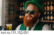 Smiling bearded man in green hat and sunglasses holding glass of beer in pub. Стоковое AI-изображение, AI-художник Дмитрий Нечаев / Фотобанк Лори