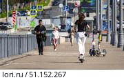 Moscow July 25 2025, People walking on the sidewalk in the city, a girl in white pants and a black T-shirt is fast riding a scooter on the sidewalk bypassing pedestrians. Редакционное фото, фотограф Скрипачев Антон / Фотобанк Лори