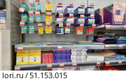 Shelves in a stationery store. The display case contains sets of plasticine, wax crayons, and creative supplies. At the top of the shelf hang bright packages of wax crayons from different manufacturers — Luch, Kroha, Karandashi-Uveseliteli, and others. Below are boxes of plasticine in bright yellow, white, and colored packages, including large sets of 18 colors. On the right side, neatly folded folders and A4 and A3 files of different colors — pink, purple, blue, and black — are visible. In the foreground are price tags with promotions, emphasizing the commercial atmosphere. The photo conveys the atmosphere of a stationery store well and is suitable for use in online catalogs, store advertising materials, articles about school supplies, and materials for children's creativity. Редакционное фото, фотограф Анна Кривицкая / Фотобанк Лори