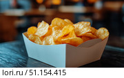 Crispy Potato Chips Served in a White Takeout Box on a Wooden Table in a Casual Dining Setting. Стоковое AI-изображение, AI-художник Юлия Гапеенко / Фотобанк Лори