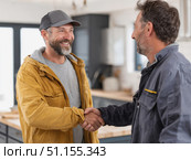 Two smiling middle-aged men shake hands in a bright modern kitchen, celebrating successful renovation work, showing satisfaction, agreement and professional accomplishment. Стоковое AI-изображение, AI-художник Катерина Бондарец / Фотобанк Лори