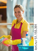 Smiling female cleaner wearing gloves and apron sanitizing glass railing indoors with cleaning supplies in a bright modern environment. Стоковое AI-изображение, AI-художник Катерина Бондарец / Фотобанк Лори