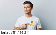 Сaucasian man stands with a yellow ribbon on a white t-shirt, pointing at it. Стоковое AI-изображение, AI-художник Екатерина Селезнева / Фотобанк Лори