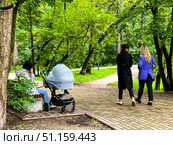 A woman in a blue jacket walks with two other women in a park. Russia. Moscow. 21.08.25. Редакционное фото, фотограф Ярославский Максим / Фотобанк Лори