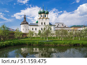 Митрополичий сад. Ростовский кремль в Ярославской области России, архитектурный ансамбль с белокаменными стенами и зелеными куполами православного храма, отражение в пруду и весенний сад на фоне голубого неба (2019 год). Редакционное фото, фотограф KOSIM / Фотобанк Лори