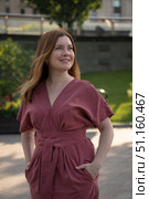 Smiling woman in a rose dress stands outdoors in soft natural light with greenery and flowers in the background. Стоковое фото, фотограф Софья Соломонова / Фотобанк Лори