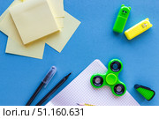 Back to School Supplies with Notebook, Fidget Spinner, Sticky Notes and Pens on Blue Background.Flat lay composition of school supplies on a blue desk. Open squared notebook with pencil, pens, sticky notes, colorful fidget spinner and highlighters. Creative back to school background, education concept, stationery for students and kids. Стоковое фото, фотограф Анастасия Мерчик / Фотобанк Лори