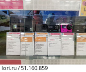 Electronics store windows with action cameras of various brands and models on display. In the foreground are Sony HDR-AS50, GoPro Fusion, GoPro Hero7 Silver Edition, Eken H9R PRO Ultra HD 4K, Eken Ultra HD 4K Pink, and budget action camera models. The cameras are presented in transparent protective boxes with price tags and specifications under each model. The price tags indicate video resolution, Wi-Fi, Time-lapse mode, smartphone control, and other functions. The photo was taken in the KEY store (Russia). The atmosphere of the photo conveys the process of choosing equipment for outdoor activities, sports, and travel. (2019 год). Редакционное фото, фотограф Анна Кривицкая / Фотобанк Лори