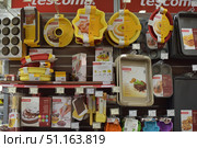 Shelves in a store with kitchen molds and baking accessories from the Tescoma brand. The display case features various silicone and metal molds for cakes, pies, cupcakes, muffins and cookies. Round, rectangular and shaped molds in bright colors are visible - yellow, red, beige and gray. The assortment also includes spatulas, brushes, pastry bags with nozzles, decorative stencils and sets for decorating baked goods. Bright packages with images of ready-made dishes emphasize the purpose of the goods. The photo conveys the atmosphere of a specialized store of kitchen goods and can be used to illustrate topics related to cooking, baking and confectionery (2015 год). Редакционное фото, фотограф Анна Кривицкая / Фотобанк Лори