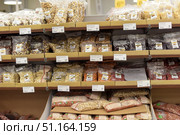 A supermarket or health food store display case with a wide selection of nuts and dried fruits. The shelves are lined with transparent plastic packages of various sizes containing cashews, almonds, peanuts, hazelnuts, mixed nuts, dried goji berries, raisins and other natural products. Each package has a sticker with information about the ingredients and the manufacturer. The price tags indicate the cost in euros for different items. The assortment is laid out in neat rows, creating the impression of abundance and variety.The image conveys the atmosphere of the nut and dried fruit department, suitable for illustrating topics related to nutrition, healthy lifestyle, veganism and natural products. (2015 год). Редакционное фото, фотограф Анна Кривицкая / Фотобанк Лори