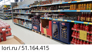 Supermarket shelves with a variety of food products. In the foreground, bottles of Felix ketchup are neatly displayed in boxes with price tags. Nearby are large packages of Barilla pasta, also displayed on pallets. In the background is a selection of canned goods, including canned fish, sauces, mustard, condiments, and Kikkoman soy sauce. The shelves are organized by category, and the products are neatly arranged, creating an atmosphere of order and abundance. The image is suitable for use in retail, grocery, marketing, trade, and consumer goods. (2019 год). Редакционное фото, фотограф Анна Кривицкая / Фотобанк Лори