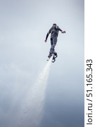 Flyboarder glides effortlessly above the water, propelled by jets of water shooting from the board. The rider wears a sleek wetsuit and maintains a steady posture, showcasing the thrill of flyboarding. Стоковое фото, фотограф Владимир Разгуляев / Фотобанк Лори