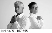 Professional mature and young businessmen standing back to back, straightening white shirts, embodying corporate teamwork and confidence. Стоковое AI-изображение, AI-художник Юрий Поздников / Фотобанк Лори