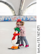 Happy little girl in warm pink coat and red safety helmet holding support and learning to skate on ice skating rink. Fall down and have fun. Winter sport, outdoors. Holiday and seasonal concept. Стоковое фото, фотограф Ирина Михайличенко / Фотобанк Лори