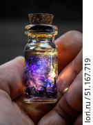 Hand holding illuminated glass jar with swirling galaxy painting, revealing miniature cosmic landscape glowing softly within delicate grasp. Стоковое AI-изображение, AI-художник Юрий Поздников / Фотобанк Лори