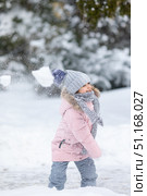 Little girl having fun playing with fresh snow during snowfall. Snowball fight. Kid dressed in warm clothes, hat, hand gloves and scarf. Active outdoors leisure for child on nature in snowy winter day. Стоковое фото, фотограф Ирина Михайличенко / Фотобанк Лори