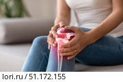 Knee pain icon. Joint pain, Arthritis and tendon problems. Woman in jeans sitting sofa, touching nee at pain point. Mature person feeling unwell, suffering from pain in leg. Red effect painful injury. Стоковое AI-изображение, AI-художник Марина Демидюк / Фотобанк Лори