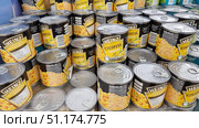 Supermarket counter with cans of Heinz sweet corn. The cans are black and yellow with a large Heinz logo and the words "Sweet Corn." The labels show corn kernels, information about the ingredients and nutritional value. The cans are visible both with the front side up and turned sideways with the lids up. The lids have tabs for easy opening. The photo illustrates the assortment of a grocery store, the packaging of canned vegetables and the mass production of food products. (2021 год). Редакционное фото, фотограф Анна Кривицкая / Фотобанк Лори