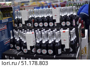 A supermarket display case with a large number of bottles of Martini Asti sparkling wine, both gift-wrapped and unwrapped. The bottles are arranged in rows on cardboard boxes, creating a neat display. Cinzano Bianco packages are visible on the left side of the frame, and other alcoholic beverages are in the background. The black and silver bottles with branded labels stand out against the store background, creating a festive atmosphere. The scene is typical of a supermarket or hypermarket, where drinks are sold in bulk before the holidays. (2015 год). Редакционное фото, фотограф Анна Кривицкая / Фотобанк Лори