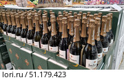 A supermarket display case with a large number of bottles of Lev Golitsyn sparkling wine in green cardboard boxes. The bottles are lined up in rows, each with gold foil on the neck and a branded label. The packaging is designed for six bottles of 0.75 liters. In the background, other products and customers are visible, which emphasizes the atmosphere of a large store. The photo perfectly illustrates the theme of alcoholic beverages, holiday shopping and trade. (2021 год). Редакционное фото, фотограф Анна Кривицкая / Фотобанк Лори