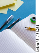Flat lay image of an open squared grid notebook placed on a blue background next to a black gel pen, a mechanical pencil, and sticky notes. Bright natural lighting and clean composition create a modern and minimalistic workspace. Perfect for educational, back to school, stationery, studying, productivity and office branding themes. Стоковое фото, фотограф Анастасия Мерчик / Фотобанк Лори
