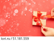 A holiday card with highlights and blurred lights, a gift in your hands, a red ribbon. Стоковое фото, фотограф Alexandra Aleroewa / Фотобанк Лори