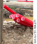 Red plastic construction pipes stacked at a muddy site, showing industrial building materials. Стоковое фото, фотограф Анастасия Золотницкая / Фотобанк Лори