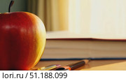 A red apple sits on a wooden desk beside a stack of books and pens, bathed in soft sunlight, creating a warm atmosphere in a study. Стоковое AI-видео, аниматор Данила Большаков / Фотобанк Лори
