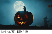 A giant jack-o'-lantern glows in the dark while someone holds a balloon, surrounded by festive decorations on a spooky Halloween night. Стоковое AI-видео, аниматор Данила Большаков / Фотобанк Лори