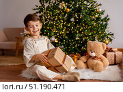 Happy little boy opens a gift box while sitting on a fur carpet near Christmas tree. Child is happy with a New Year gift. The concept of Christmas and New Year holidays. High quality photo. Стоковое фото, фотограф Ирина Михайличенко / Фотобанк Лори